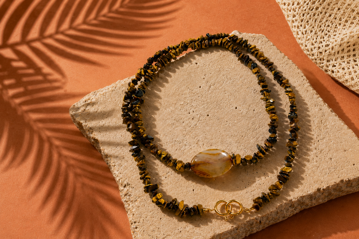 Tiger eye chip necklace with a banded agate stone, resting on travertine against terracotta with palm shadows